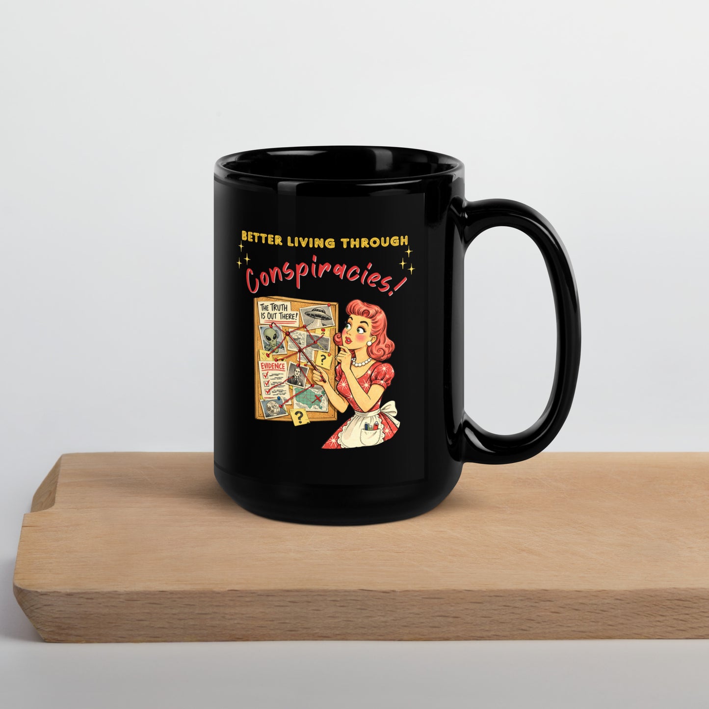 Better Living Through Conspiracies black ceramic mug — vintage 1950s retro housewife pointing at alien evidence cork board with red string and UFO photos, printed on both sides by Cinderpoint Studios