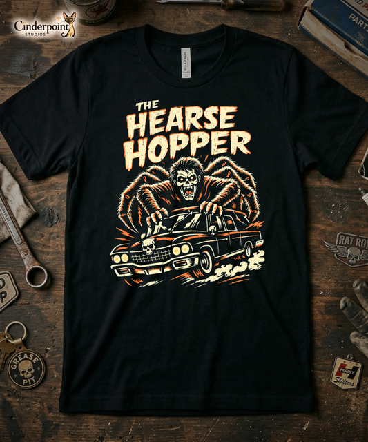 Top-down flat lay of a black Bella Canvas 3001 t-shirt with 'The Hearse Hopper' design on a rustic wooden workshop table with a wrench, spark plug, and vintage car club patches.
