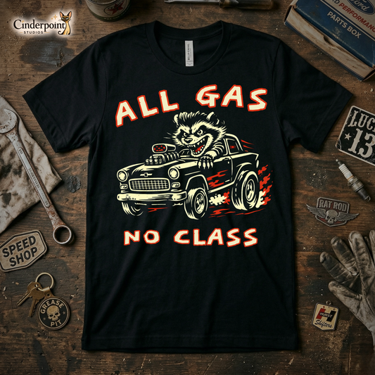 A top-down photograph of a premium black t-shirt on a weathered wooden workbench. The shirt features a two-color distressed graphic of a pompadoured raccoon driving a high-performance rat rod with the text "ALL GAS NO CLASS." Surrounding the shirt are vintage garage tools, a rusty wrench, a spark plug, and a "Grease Pit" leather keychain.
