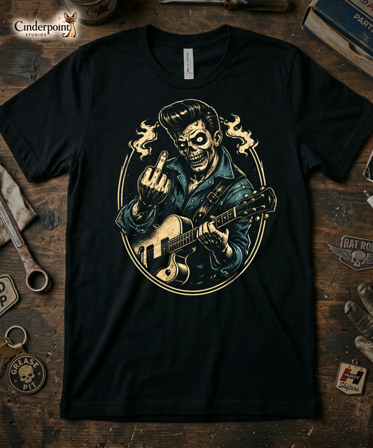 Black Bella Canvas 3001 t-shirt featuring the 'Johnny Smash' lowbrow art design. A bone-cream and midnight-blue graphic of a zombie rockabilly singer giving a middle finger gesture. Professional retail display on a vintage wooden workbench with 'Grease Pit' shop accessories.