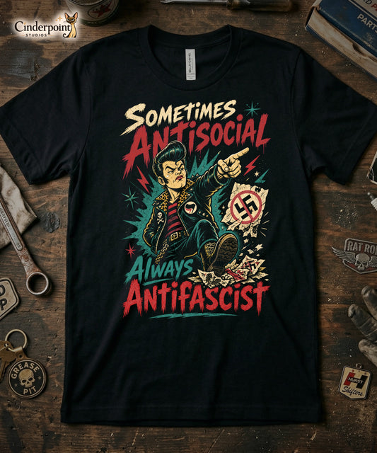 A gritty, lowbrow illustration on a black t-shirt of a pompadoured greaser in a leopard-print lined leather jacket, kicking over hate symbols. Text reads 'Sometimes Antisocial Always Antifascist' in a distressed punk-style font.