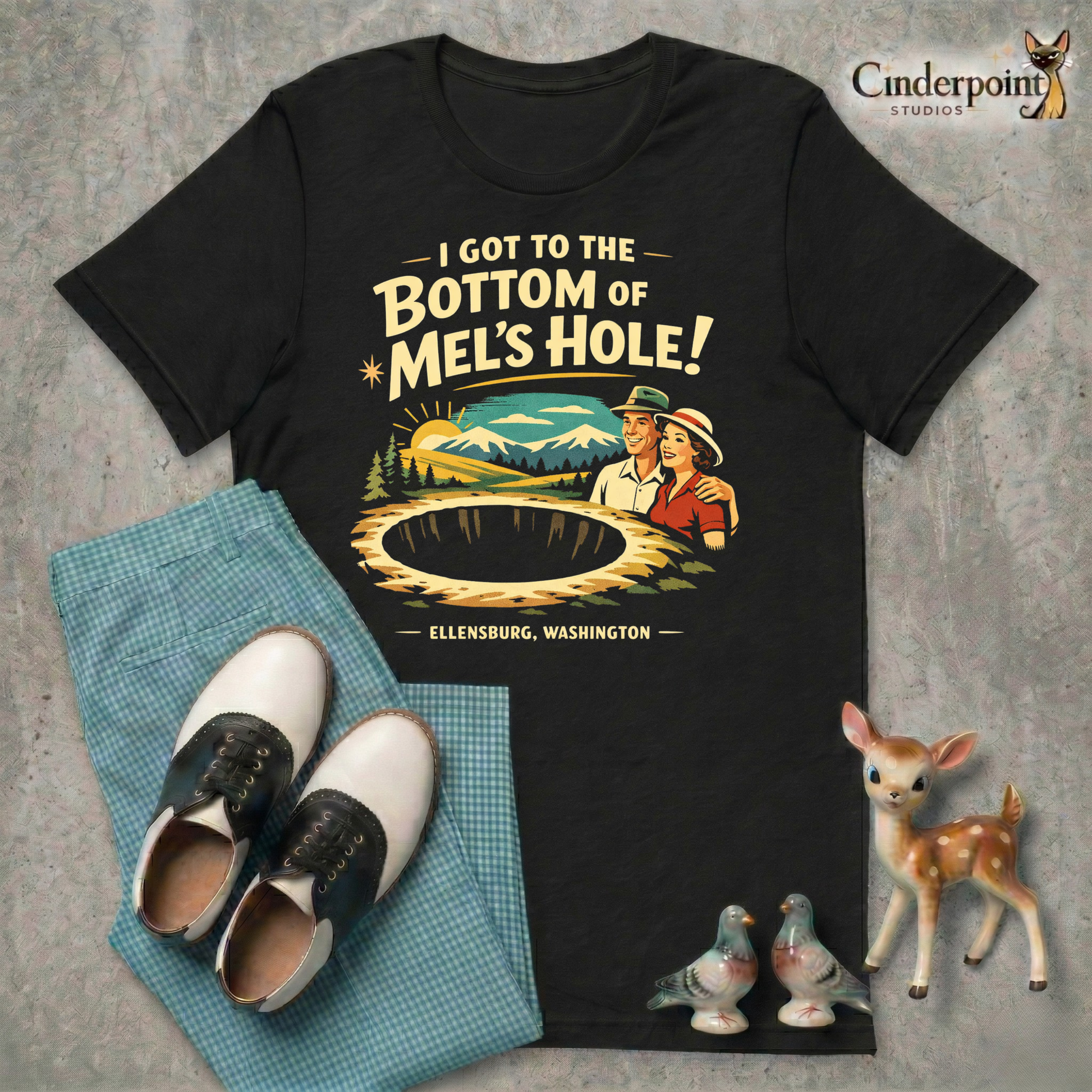 Black retro graphic t-shirt featuring a vintage travel-style illustration of smiling tourists beside a giant mysterious hole with the phrase I Got to the Bottom of Mel’s Hole and Ellensburg, Washington.