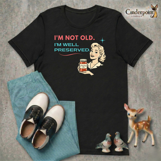 Black retro graphic t-shirt featuring a smiling vintage-inspired woman holding a jar of strawberry jam with the phrase I’m Not Old, I’m Well Preserved in coral and aqua lettering.