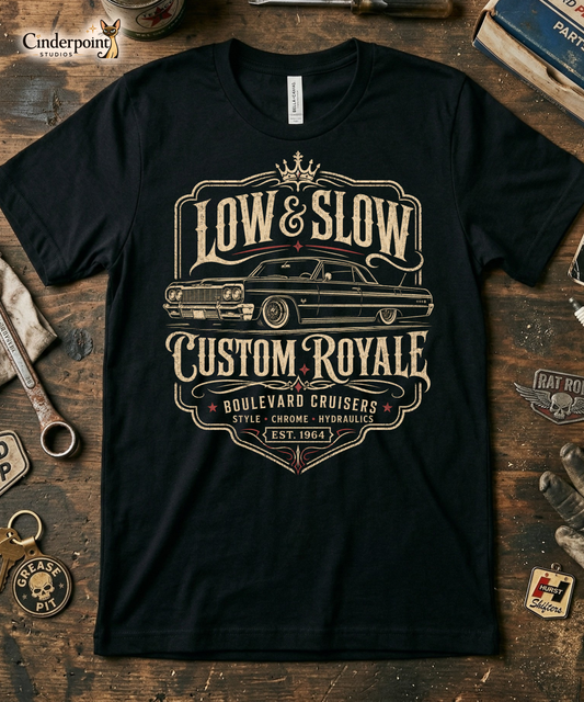 Workbench with a black graphic tee featuring original Cinderpoint Studios artwork for Low & Slow Custom Royale, a retro lowrider design with a long custom cruiser inspired by a 1964 Impala, bold vintage lettering, crown detail, elegant framing, and Boulevard Cruisers text.