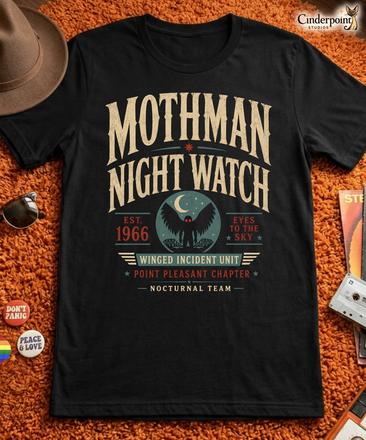 Black graphic tee featuring original Cinderpoint Studios artwork for Mothman Night Watch, a retro cryptid design with bold vintage lettering, Mothman silhouette, red eyes, crescent moon, bridge scene, and text including Winged Incident Unit, Point Pleasant Chapter, and Nocturnal Team.
