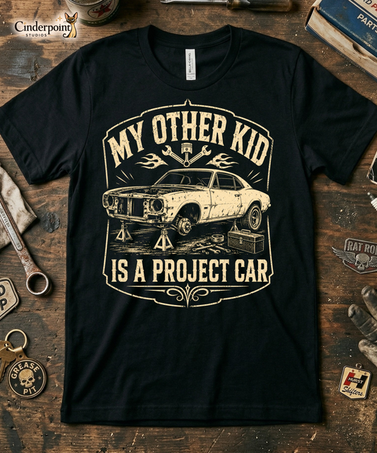 Black graphic tee featuring original Cinderpoint Studios artwork for My Other Kid Is a Project Car, a one-color retro garage design with a classic project car on jack stands, tools, piston and wrench accents, flames, and bold vintage lettering.
