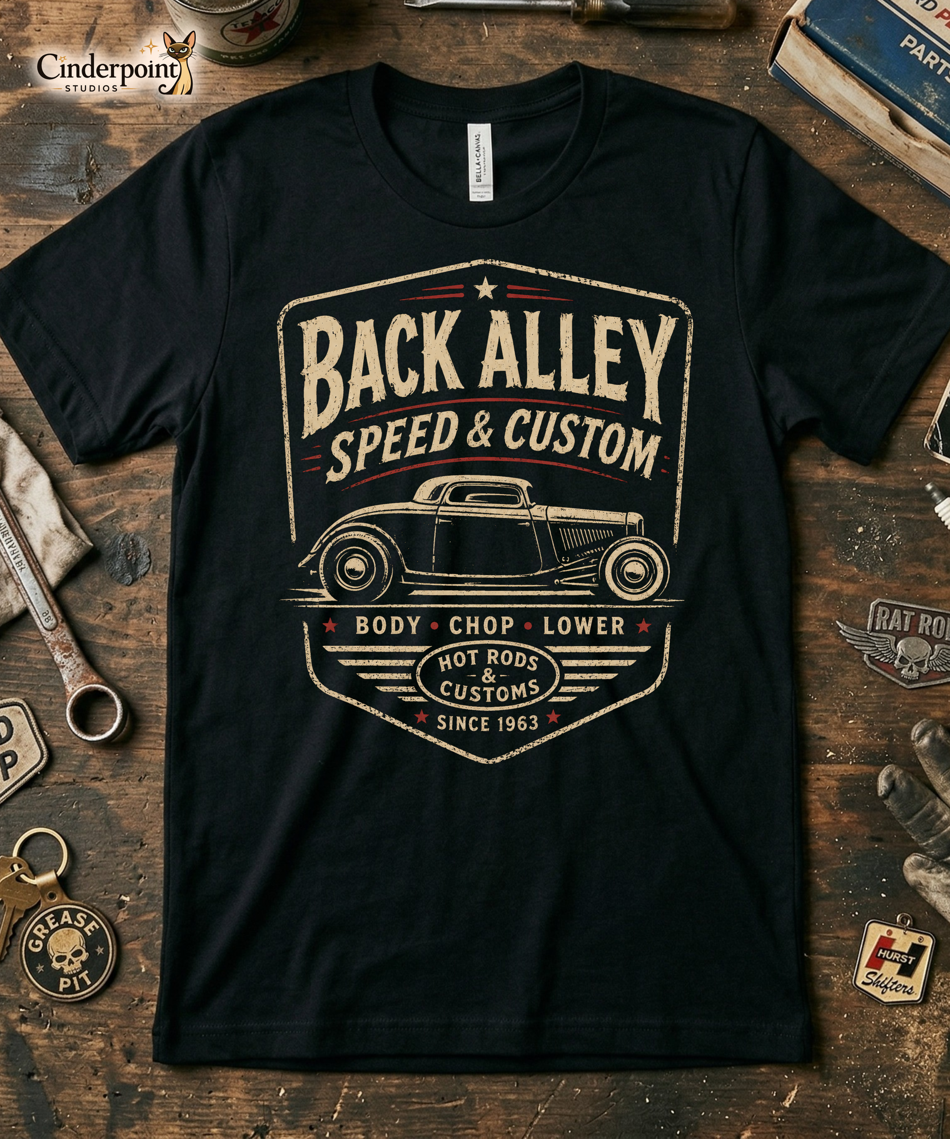 Workbench with a black graphic tee featuring original Cinderpoint Studios artwork for Back Alley Speed & Custom, a retro hot rod garage design with a chopped custom car profile, bold distressed lettering, red accent details, Body Chop Lower text, and Hot Rods & Customs badge.