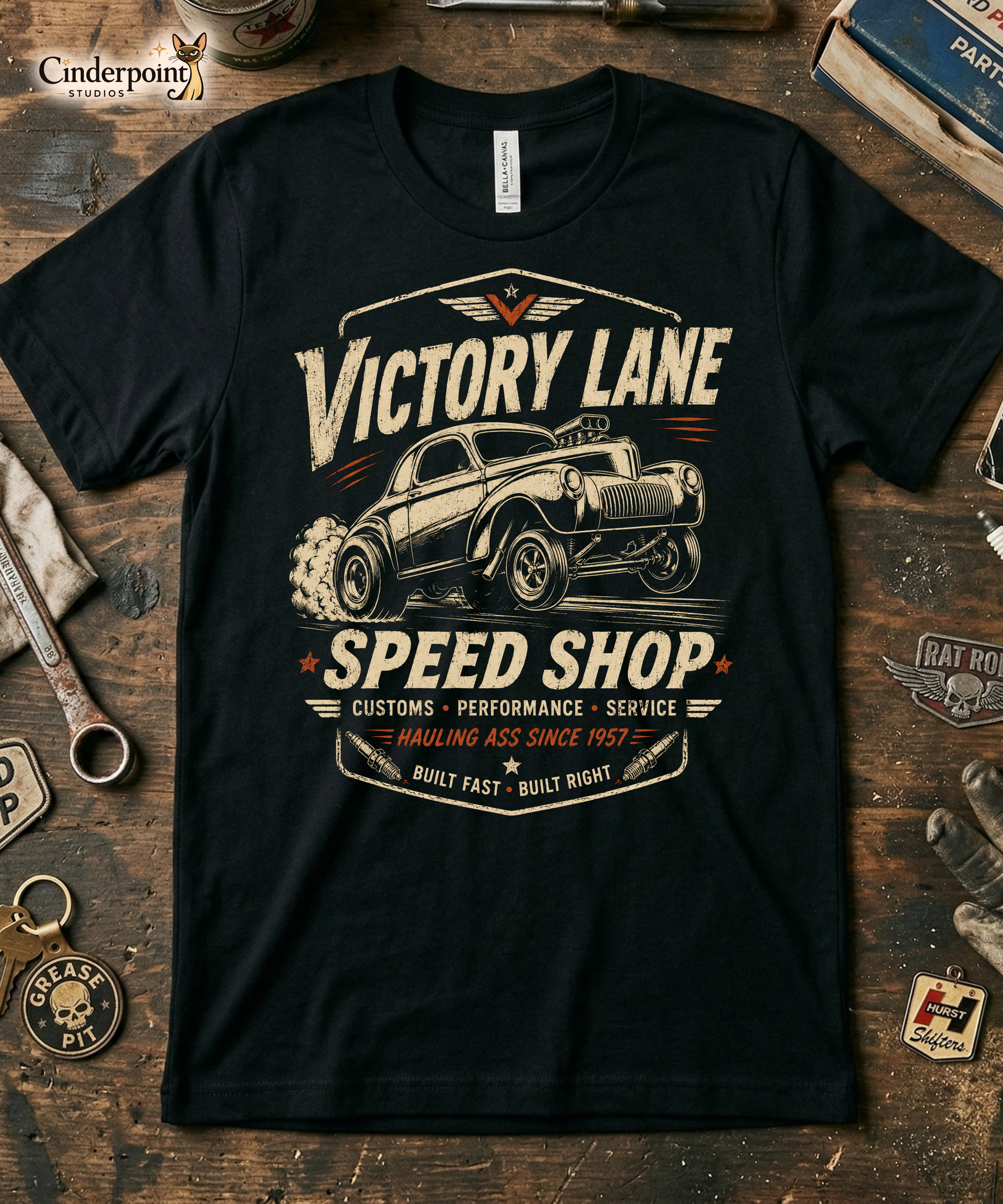 Black graphic tee featuring original Cinderpoint Studios artwork for Victory Lane Speed Shop, a retro hot rod design with a gasser-style car launching hard, bold vintage lettering, spark plug accents, orange speed details, and Built Fast Built Right text.