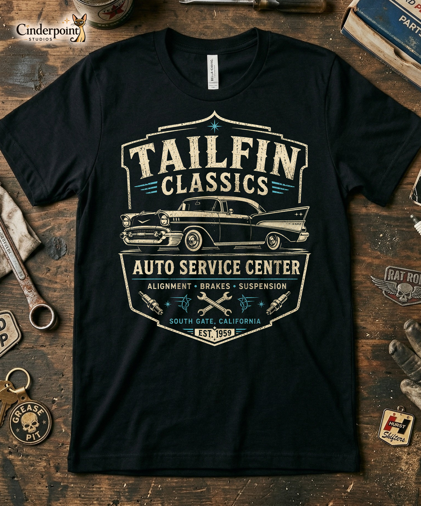 Black graphic tee featuring original Cinderpoint Studios artwork for Tailfin Classics, a retro auto service center design with a 1950s-style classic car, bold tailfins, vintage lettering, teal accents, crossed wrenches, spark plugs, and Alignment Brakes Suspension text.