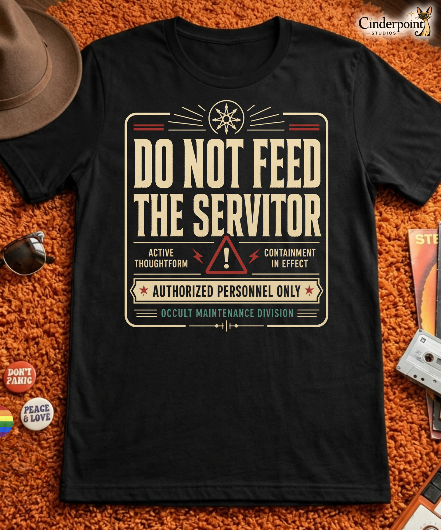 Black graphic tee featuring original Cinderpoint Studios artwork for Do Not Feed the Servitor, a retro occult warning-sign design with bold vintage lettering, a chaos star symbol, a hazard icon, and text including Active Thoughtform, Containment in Effect, Authorized Personnel Only, and Occult Maintenance Division.
