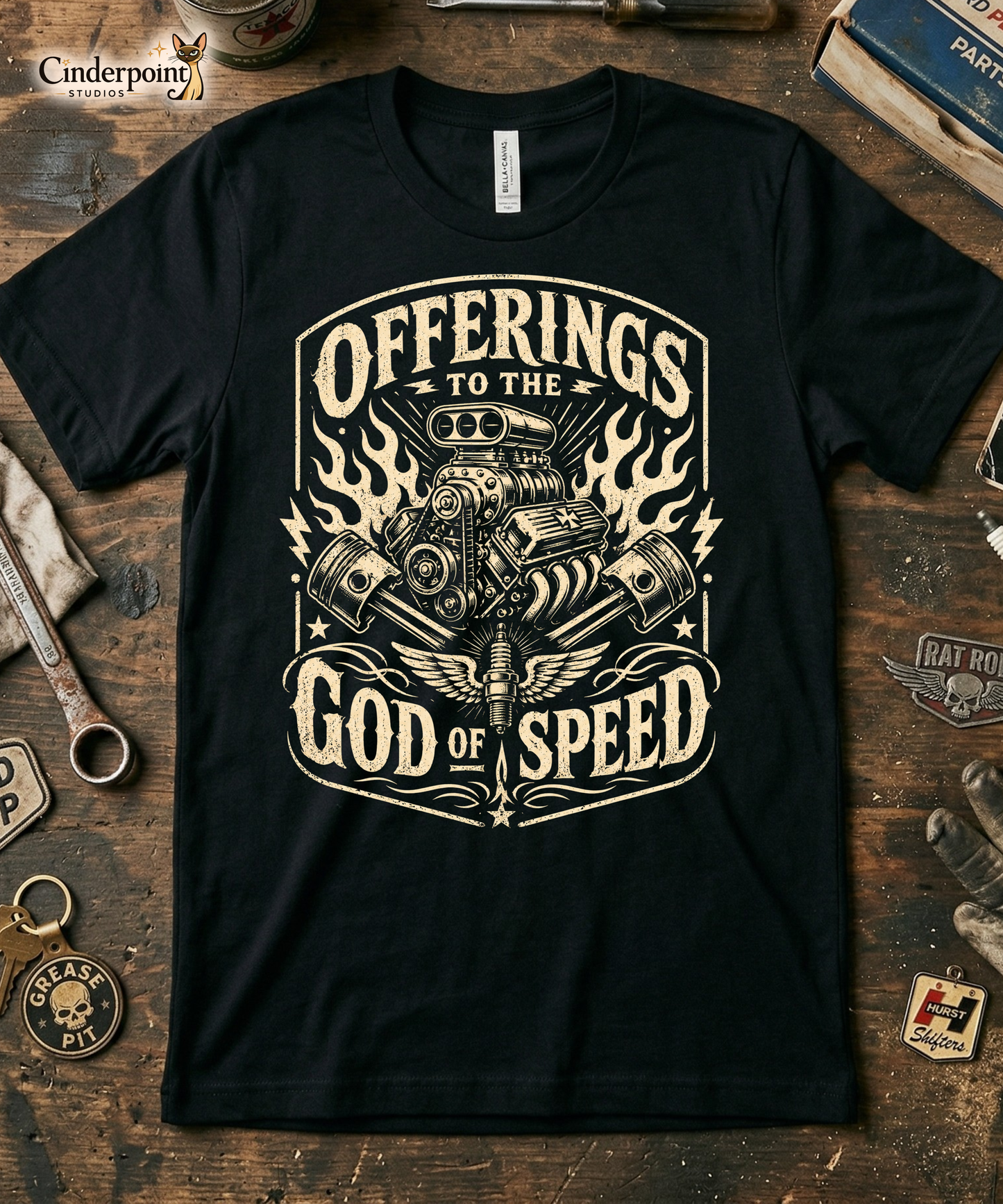 Black graphic tee featuring original Cinderpoint Studios artwork for Offerings to the God of Speed, a one-color retro gearhead design with a supercharged V8 engine, crossed pistons, winged spark plug, flames, lightning bolts, and vintage hot rod lettering.
