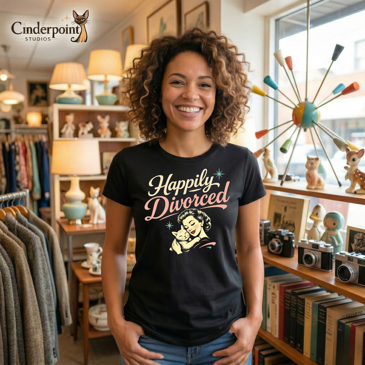 Black retro graphic t-shirt featuring the phrase Happily Divorced in cream and pink script above a vintage-inspired woman cuddling her cat with small aqua atomic starbursts.