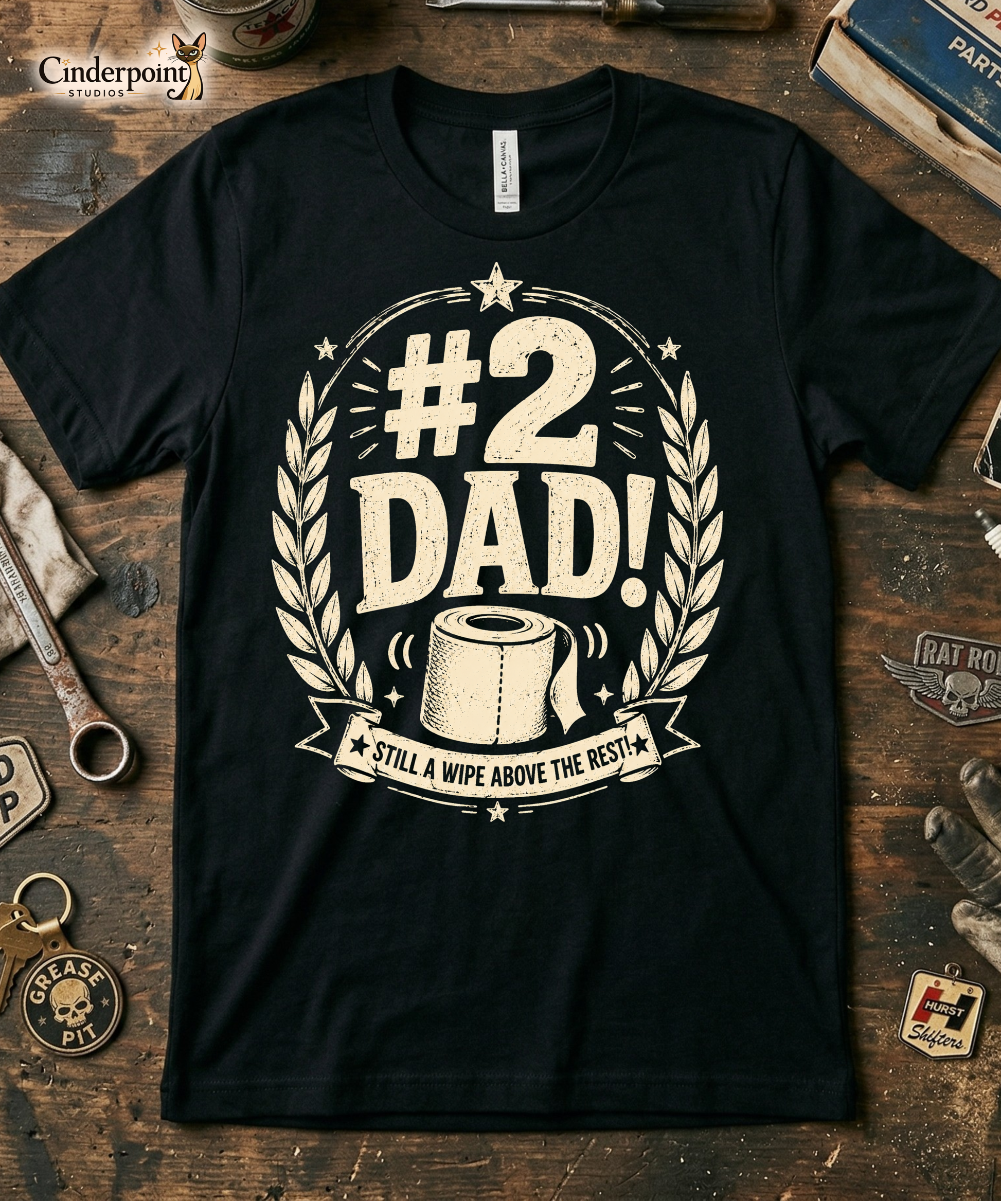 Black graphic tee featuring original Cinderpoint Studios artwork for #2 Dad, a one-color funny dad design with bold retro lettering, laurel accents, stars, a toilet paper roll illustration, and the phrase Still a Wipe Above the Rest!