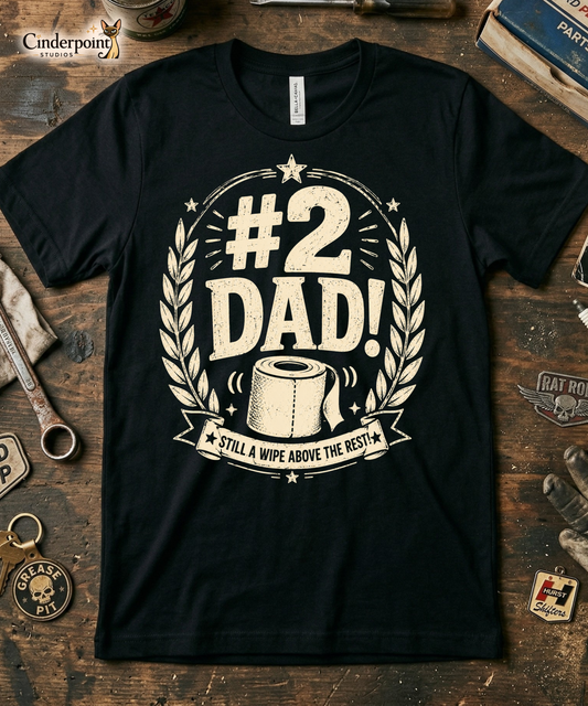 Black graphic tee featuring original Cinderpoint Studios artwork for #2 Dad, a one-color funny dad design with bold retro lettering, laurel accents, stars, a toilet paper roll illustration, and the phrase Still a Wipe Above the Rest!