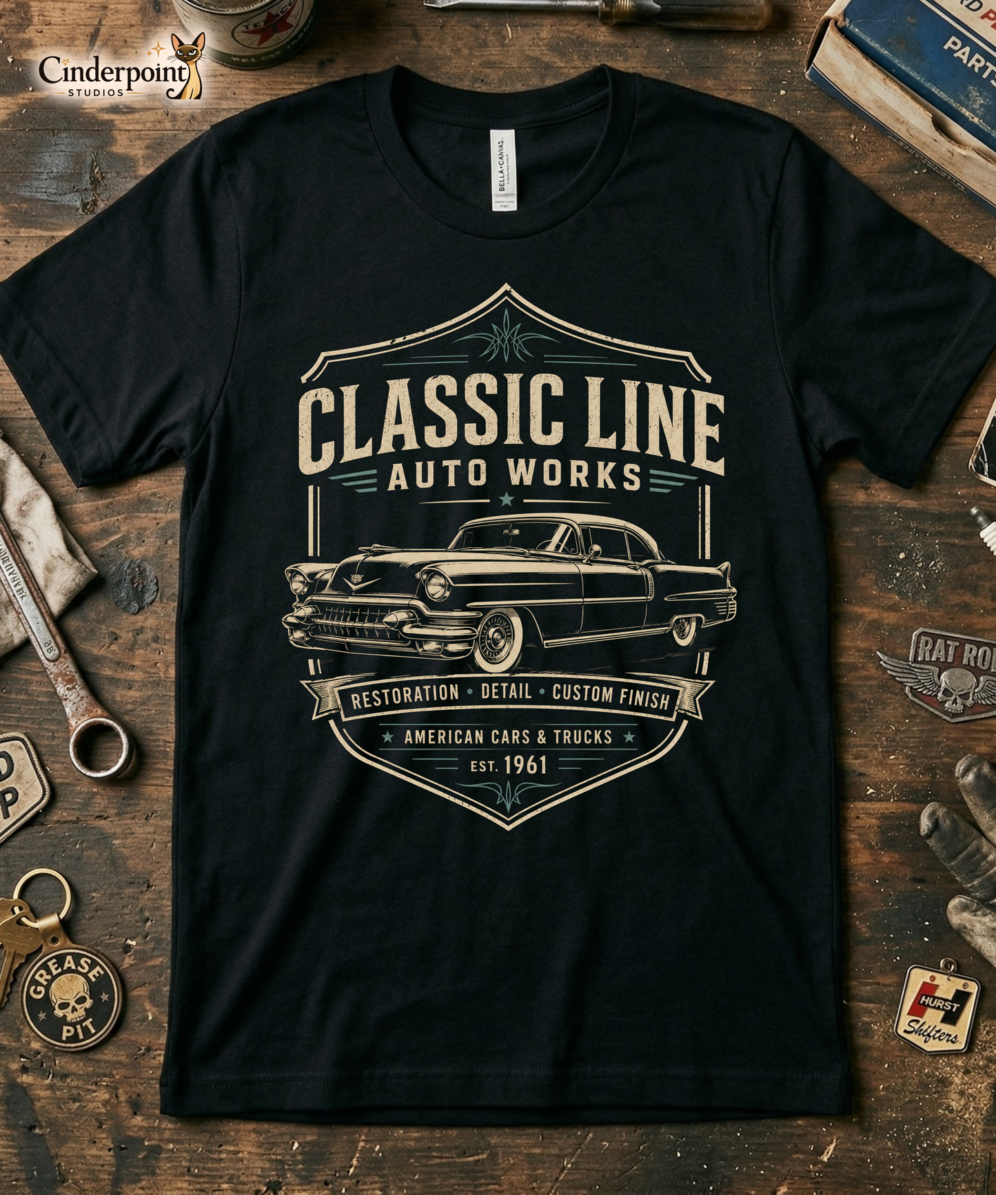 Workbench with a black graphic tee featuring original Cinderpoint Studios artwork for Classic Line Auto Works, a vintage restoration shop design with a 1950s-style classic car, bold lettering, badge-style frame, and text including Restoration Detail Custom Finish and American Cars & Trucks.