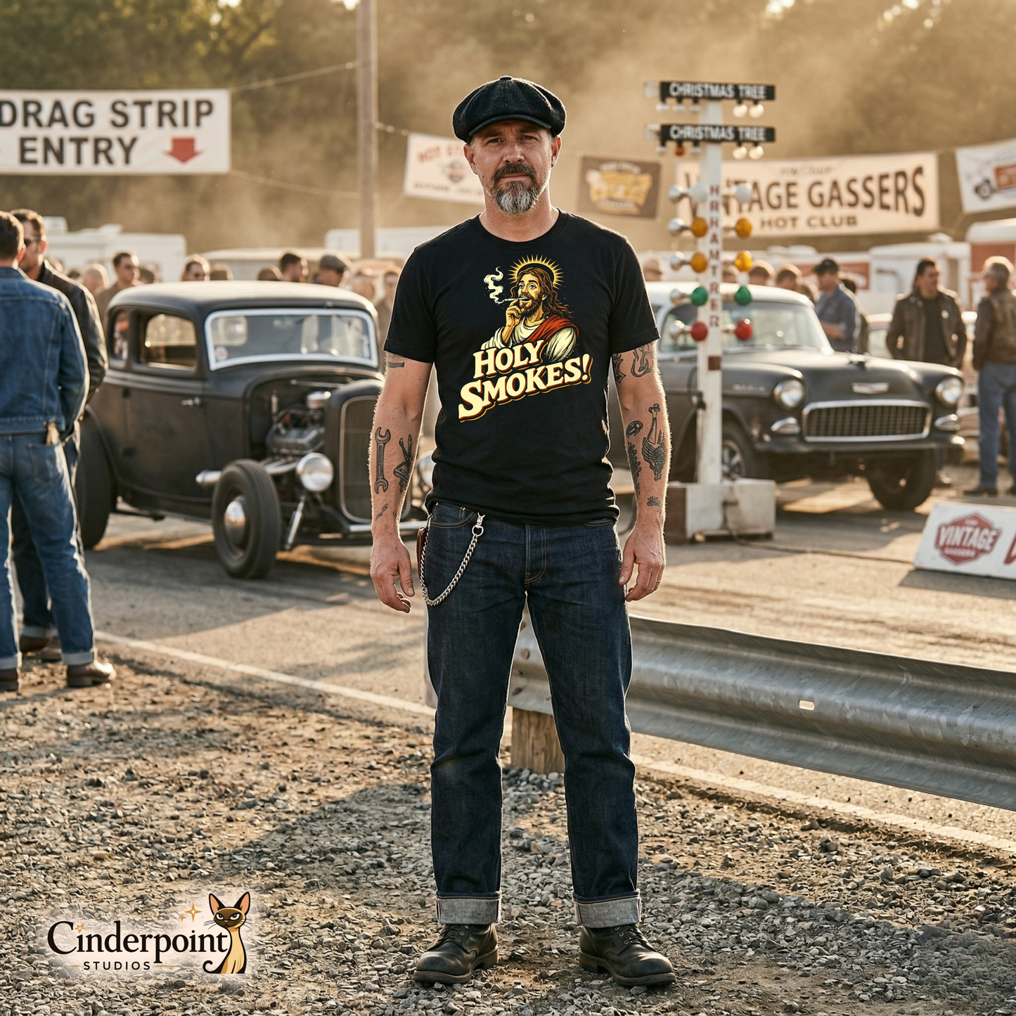 A medium shot of a man with a flat cap and tattoos wearing the "Holy Smokes!" black t-shirt, standing near a vintage gasser at a sun-drenched drag strip.