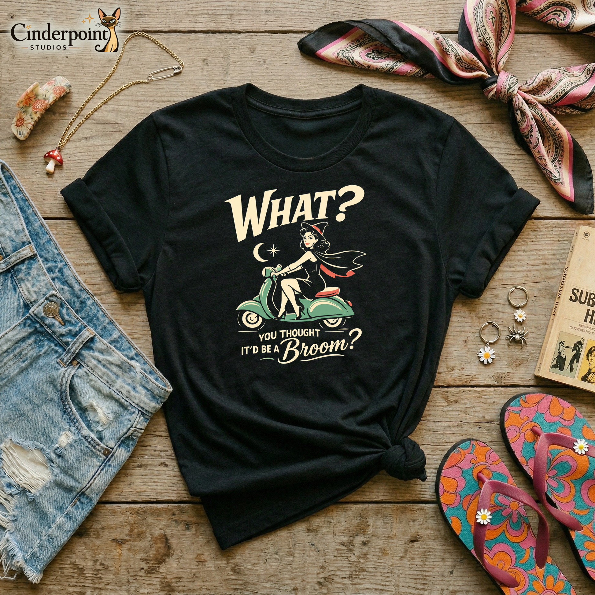 Black retro graphic t-shirt featuring a vintage-inspired witch riding a mint Vespa with the phrase What? You Thought It’d Be a Broom? in cream lettering.