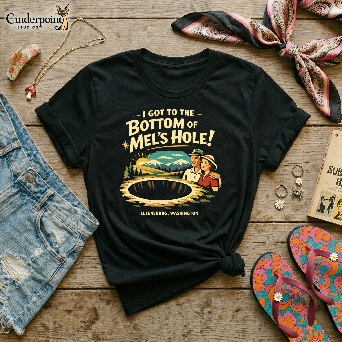Black retro graphic t-shirt featuring a vintage travel-style illustration of smiling tourists beside a giant mysterious hole with the phrase I Got to the Bottom of Mel’s Hole and Ellensburg, Washington.