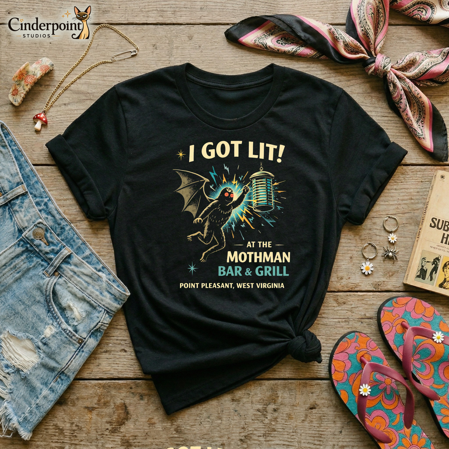 Black retro graphic t-shirt featuring Mothman flying into a glowing bug light with the phrase I Got Lit at the Mothman Bar and Grill, Point Pleasant, West Virginia.