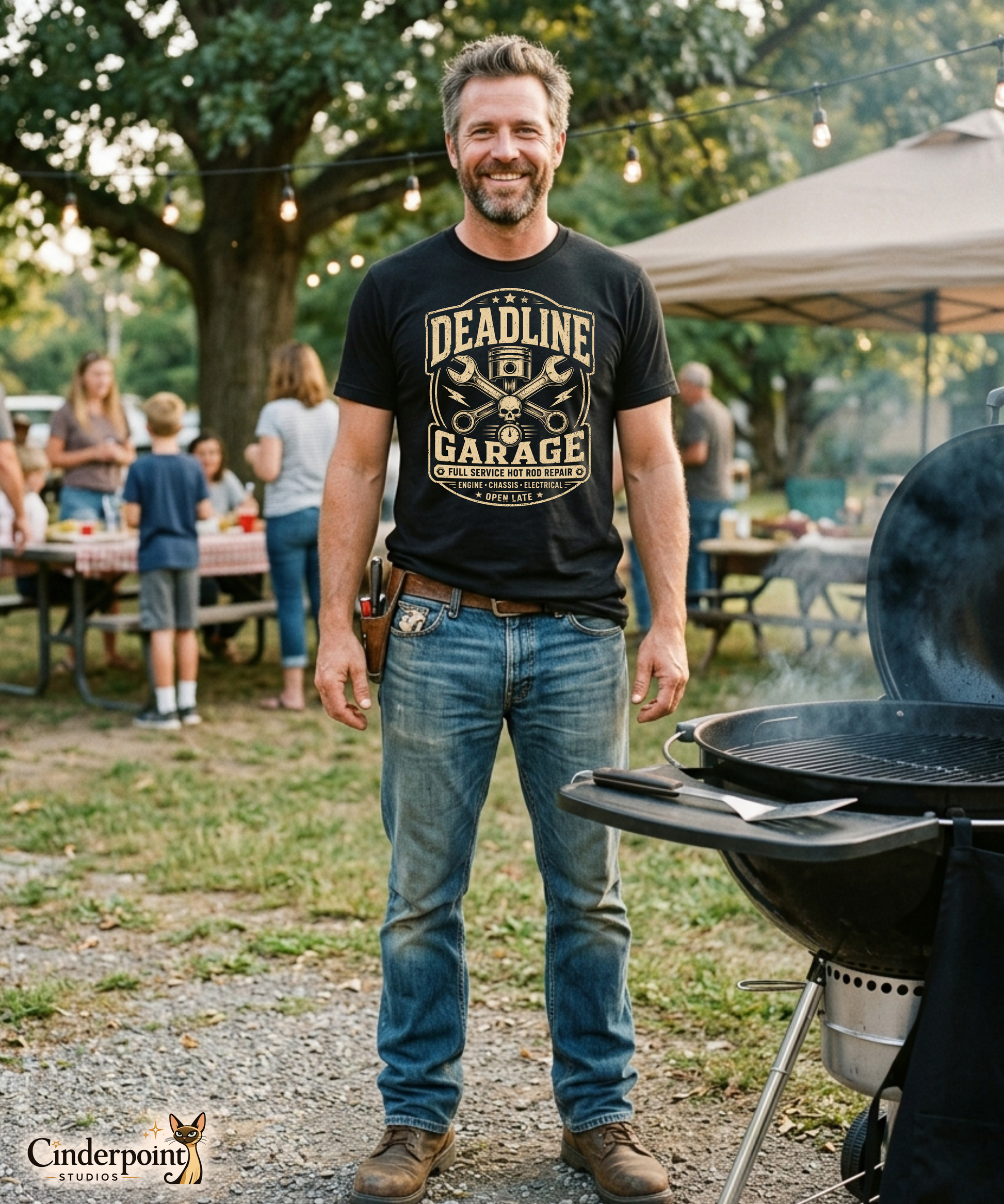 Man at a cookout wearing a black graphic tee featuring original Cinderpoint Studios artwork for Deadline Garage, a one-color retro hot rod repair design with bold lettering, piston, crossed wrenches, skull detail, lightning bolts, stopwatch accent, and Full Service Hot Rod Repair text.
