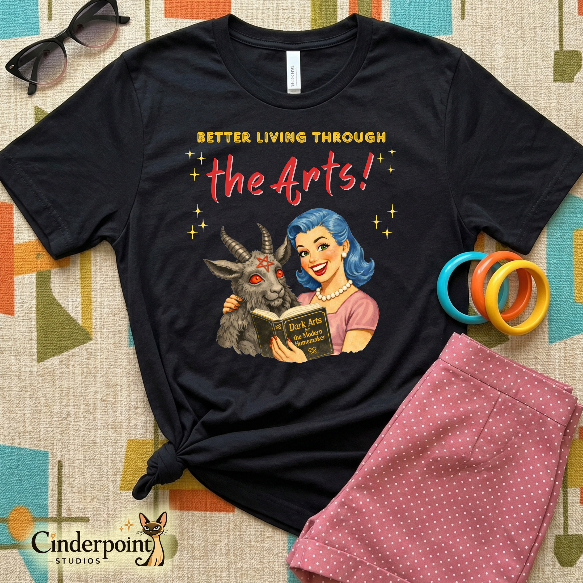 Black t-shirt with graphic design and text 'Better Living Through the Arts!' on a patterned surface.