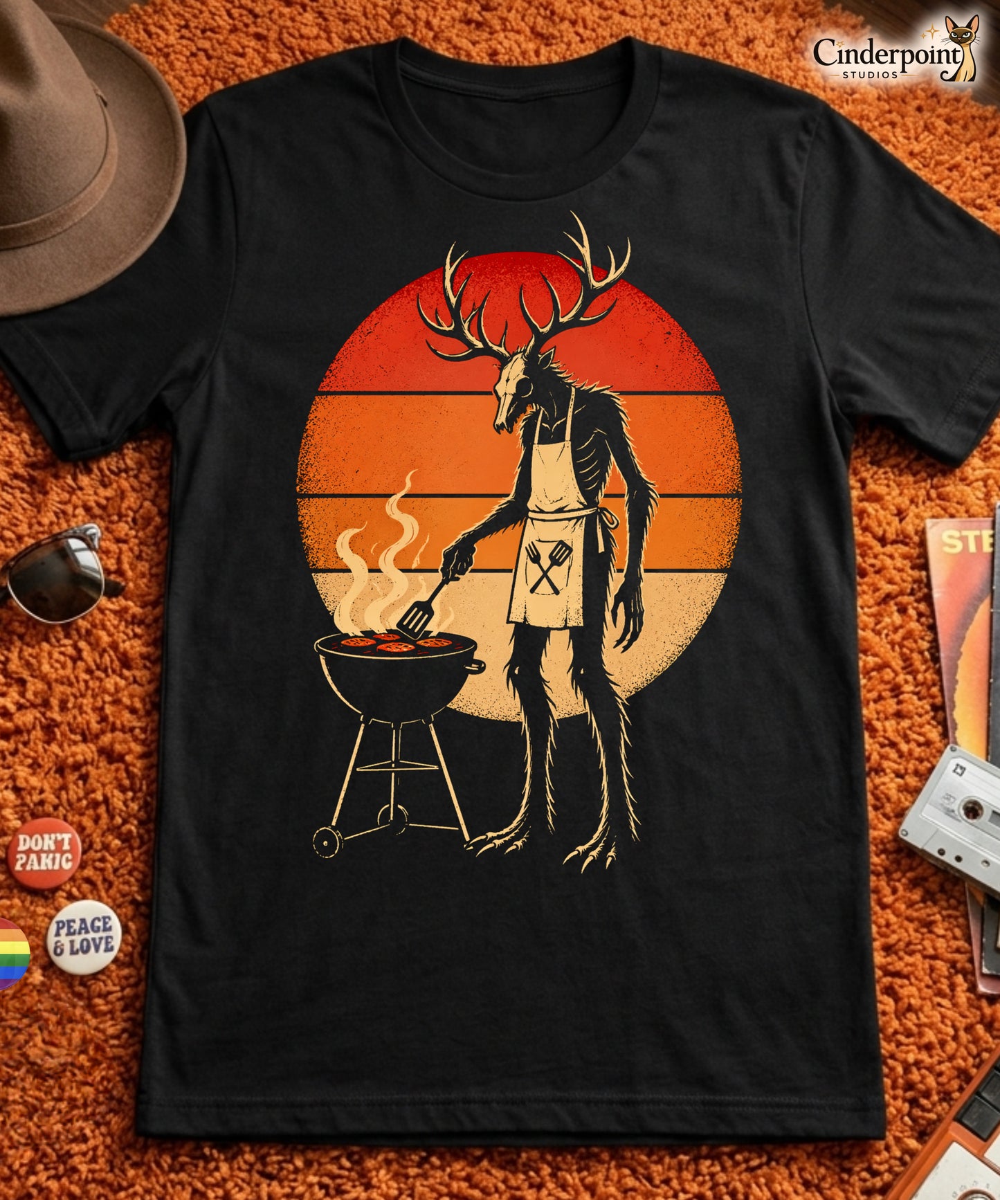 A retro-style graphic t-shirt featuring a Wendigo cryptid with antlers wearing a BBQ apron and grilling at a spatula, set against a vibrant 1980s neon sunset background.