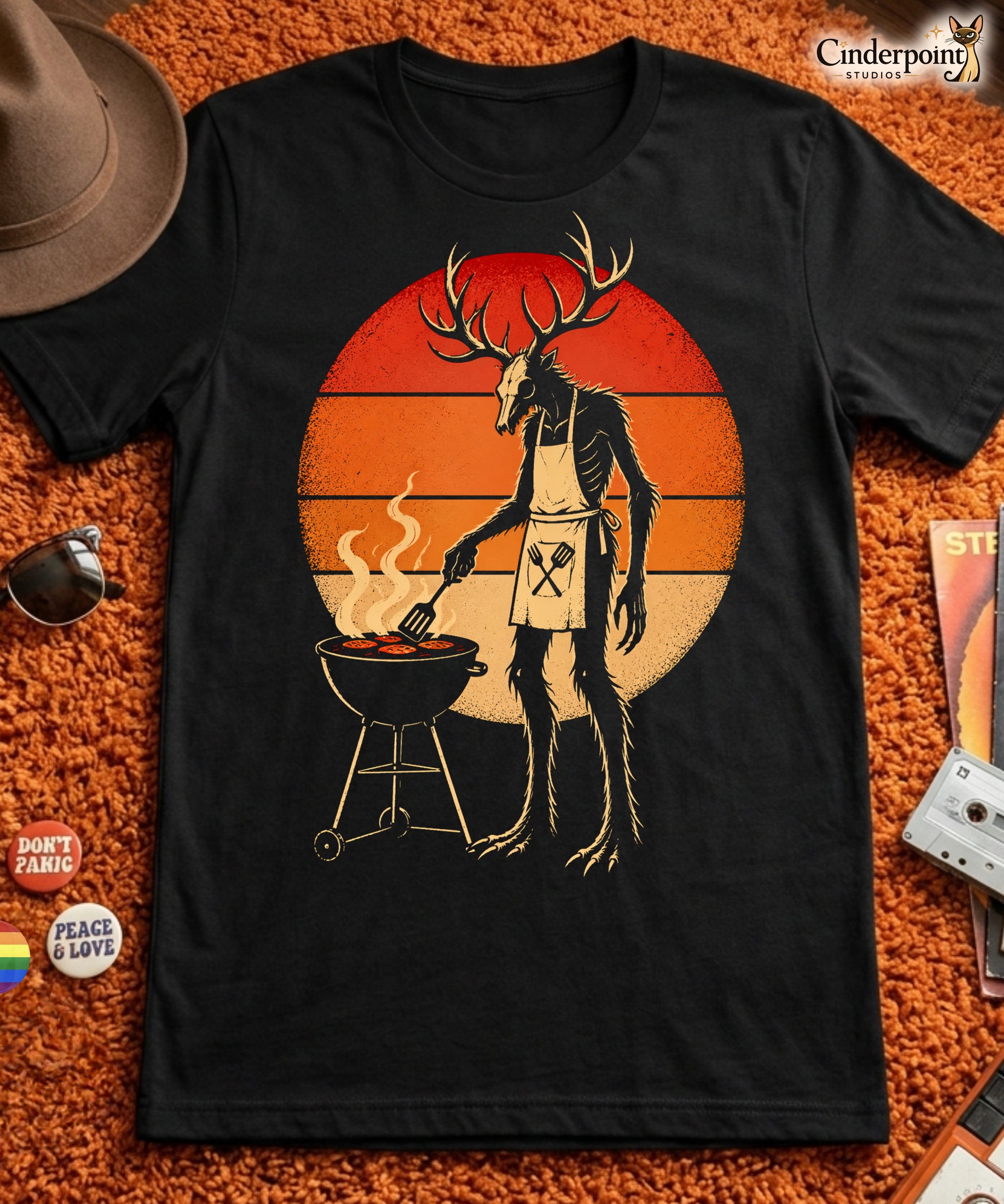 A retro-style graphic t-shirt featuring a Wendigo cryptid with antlers wearing a BBQ apron and grilling at a spatula, set against a vibrant 1980s neon sunset background.