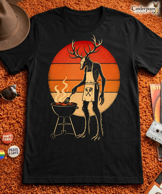 A retro-style graphic t-shirt featuring a Wendigo cryptid with antlers wearing a BBQ apron and grilling at a spatula, set against a vibrant 1980s neon sunset background.