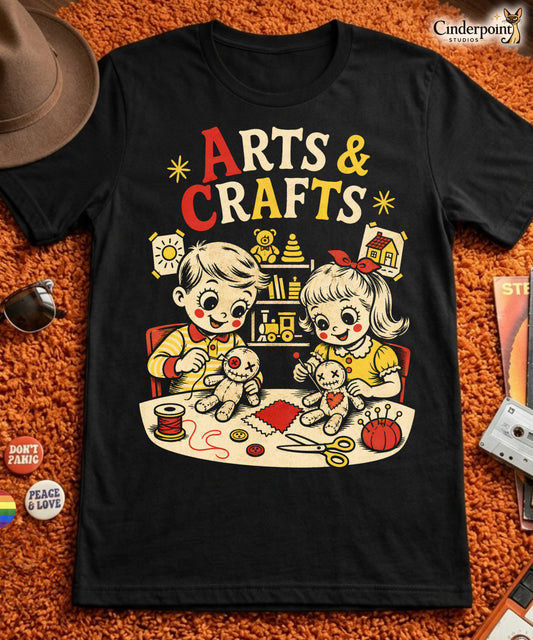 A retro-style graphic t-shirt featuring a creepy-cute voodoo doll with "Arts & Crafts" in stylized, vintage-inspired lettering, perfect for dark humor and goth fans.