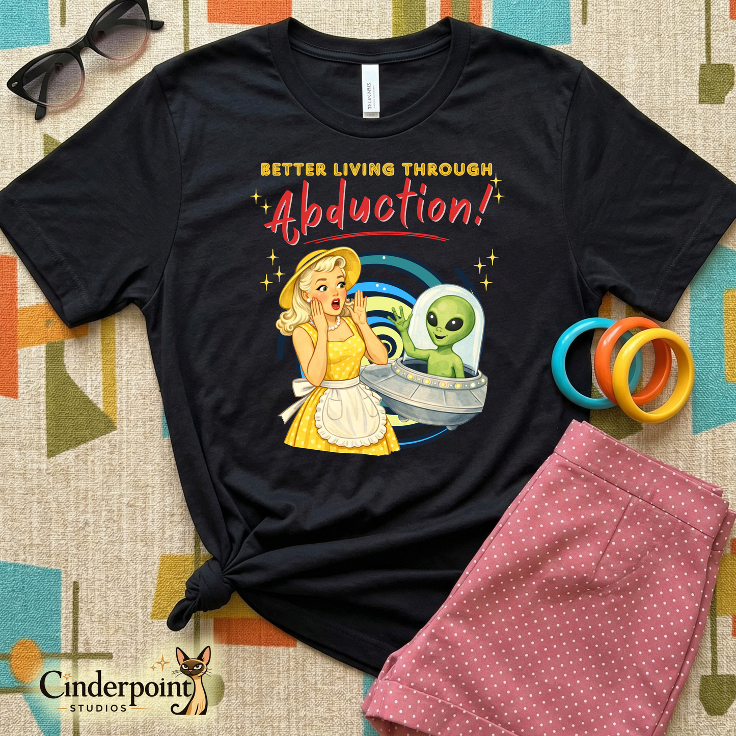 Retro watercolor illustration of a 1950s woman in a yellow polka dot dress waving at a friendly green alien in a UFO on a black t-shirt.
