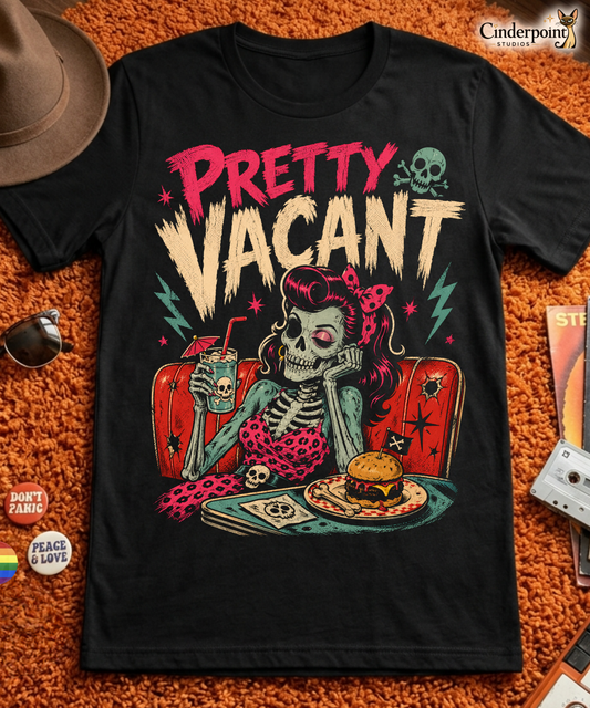 A retro-style graphic on a black t-shirt of a female skeleton pinup with pink hair in a diner booth, holding a skull-themed milkshake next to a burger with a crossbones flag.