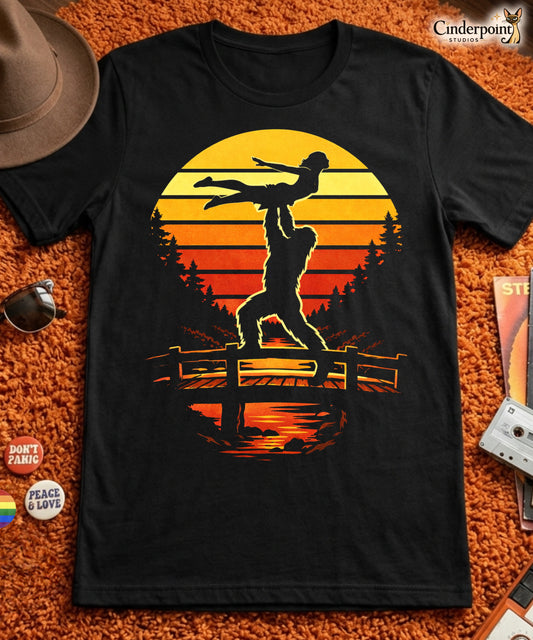 A retro-style graphic t-shirt featuring the cryptid Bigfoot performing the iconic Dirty Dancing lift pose against a vibrant, multi-colored 80s sunburst background.