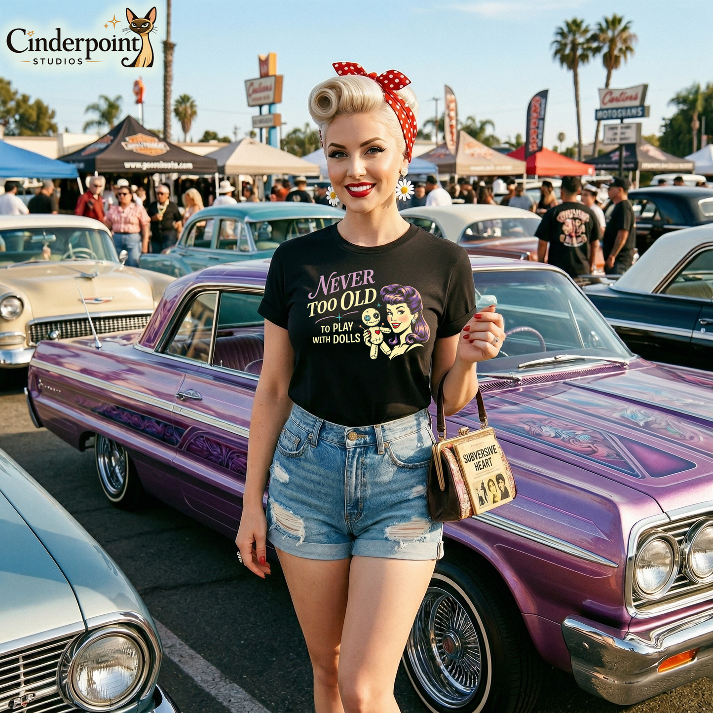 A rockabilly woman wearing a Black retro graphic t-shirt featuring the phrase Never Too Old to Play with Dolls beside a vintage-inspired woman with purple hair holding a stitched voodoo doll.