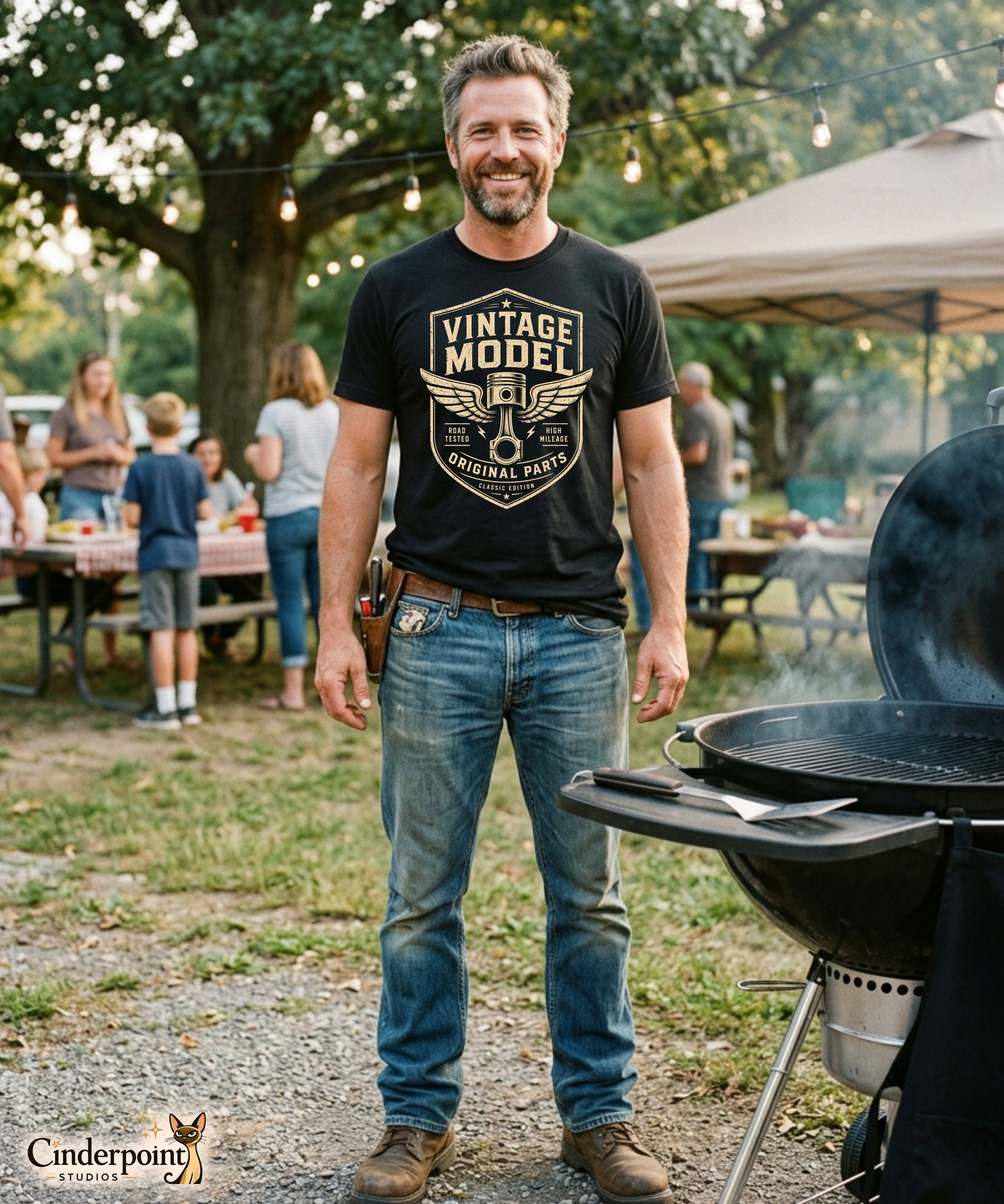 Man wearing a black graphic tee featuring original Cinderpoint Studios artwork for Vintage Model, a one-color retro garage badge design with bold lettering, a winged piston, and text including Road Tested, High Mileage, Original Parts, and Classic Edition.