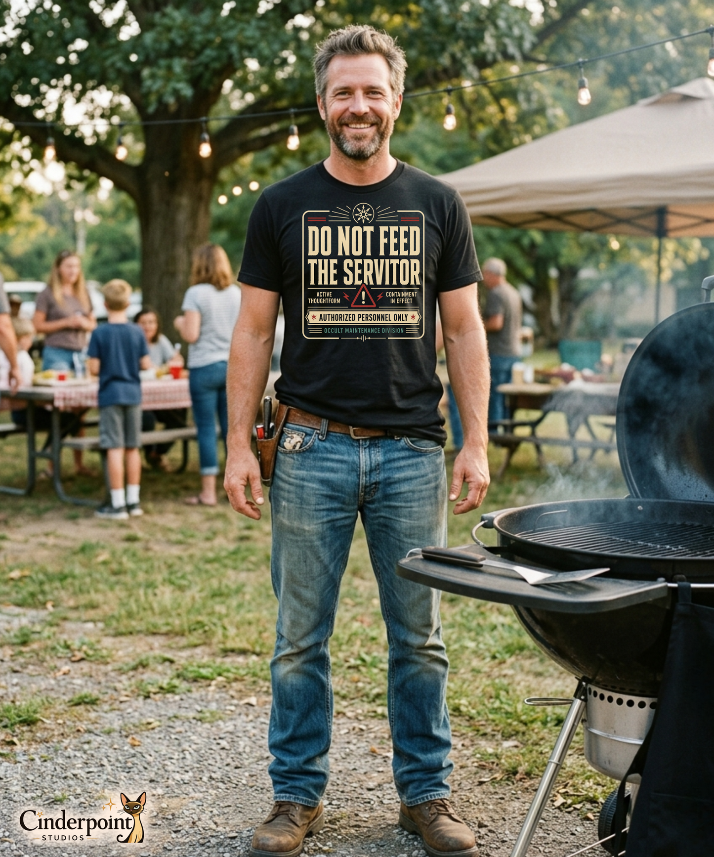A man at a cookout wearing a black graphic tee featuring original Cinderpoint Studios artwork for Do Not Feed the Servitor, a retro occult warning-sign design with bold vintage lettering, a chaos star symbol, a hazard icon, and text including Active Thoughtform, Containment in Effect, Authorized Personnel Only, and Occult Maintenance Division.