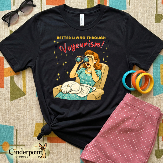 Black t-shirt with a graphic design featuring a woman with binoculars and text 'Better Living Through Vogeurism' on a patterned surface.