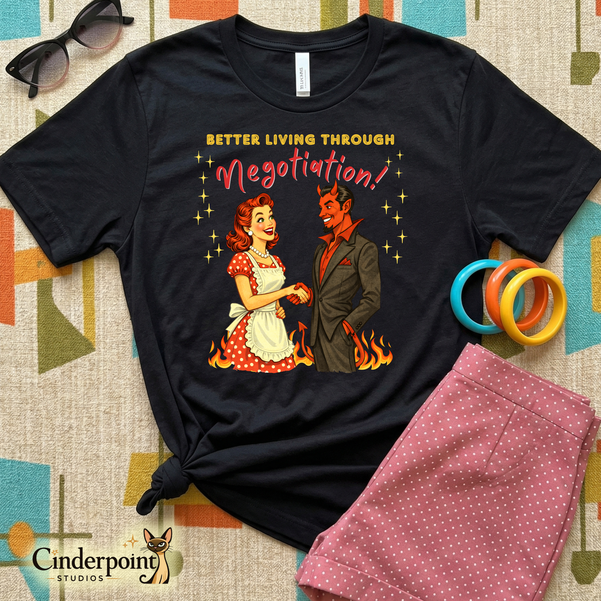 Black t-shirt with graphic design of a woman and devil holding hands with text 'Better Living Through Negotiation' on a patterned surface.