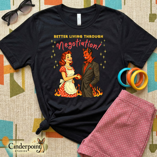 Black t-shirt with graphic design of a woman and devil holding hands with text 'Better Living Through Negotiation' on a patterned surface.