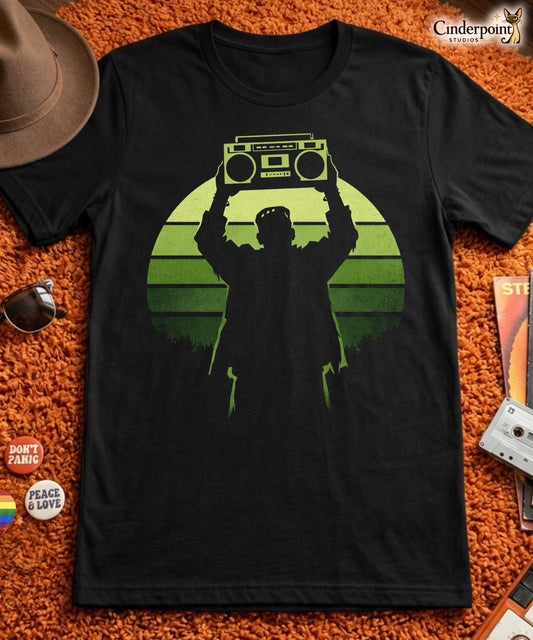 A retro-style graphic t-shirt featuring Frankenstein’s monster holding a 1980s boombox over his head in the iconic Say Anything movie pose, set against a vibrant neon sunburst.