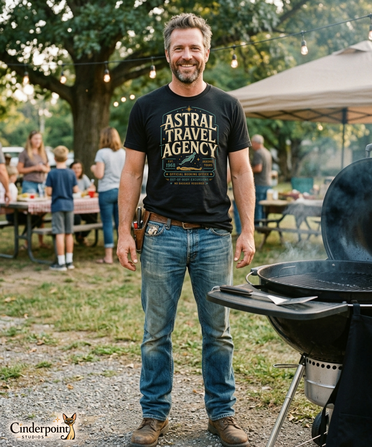 Man wearing a black graphic tee featuring original Cinderpoint Studios artwork for Astral Travel Agency, a retro occult travel design with large vintage lettering, astral projection imagery, stars, and text including Official Booking Office, Akashic Tours, and Out-of-Body Excursions.
