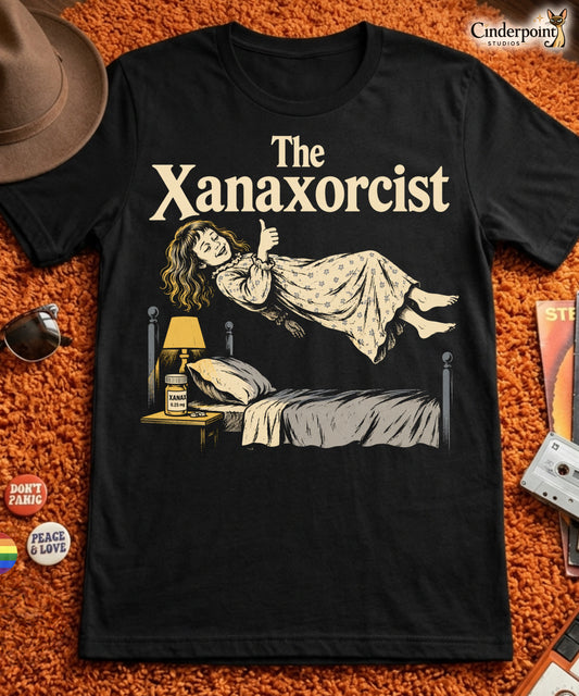 A retro horror-style graphic t-shirt featuring "The Xanaxorcist" in classic cinematic lettering with a stylized, eerie parody of the iconic exorcism scene.
