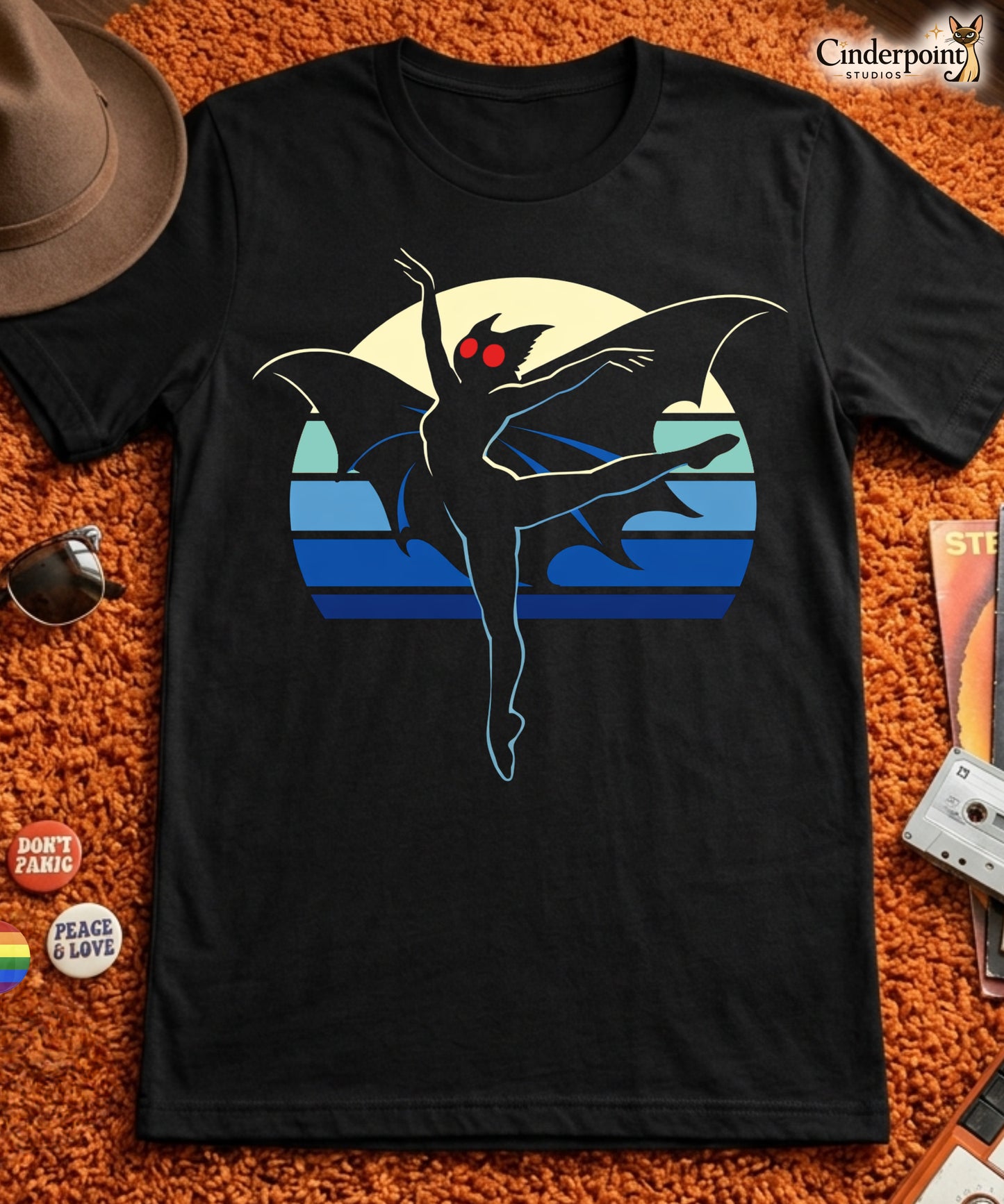 A retro-style graphic t-shirt featuring the winged cryptid Mothman in a ballet dance pose wearing a tutu, set against a vibrant neon 80s sunburst background.