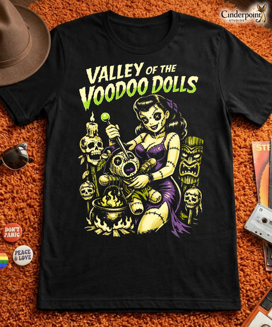 A retro-style graphic on a black t-shirt featuring a stylized pinup girl voodoo doll turning the tables on a medicine man in a vibrant, gritty Tiki-horror aesthetic
