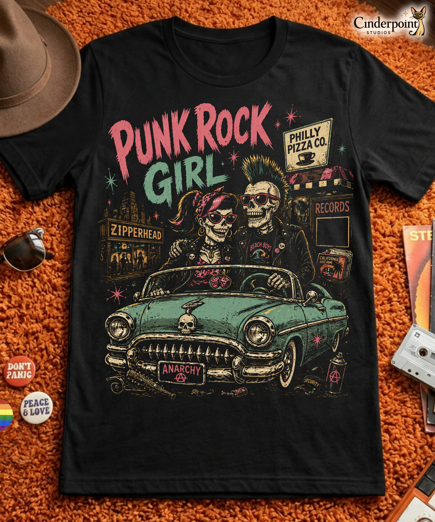 A retro-style graphic on a black t-shirt featuring two skeletons—a male with a mohawk and a female with a pink bow—driving a teal 1955 Chevy past iconic Philadelphia punk landmarks.
