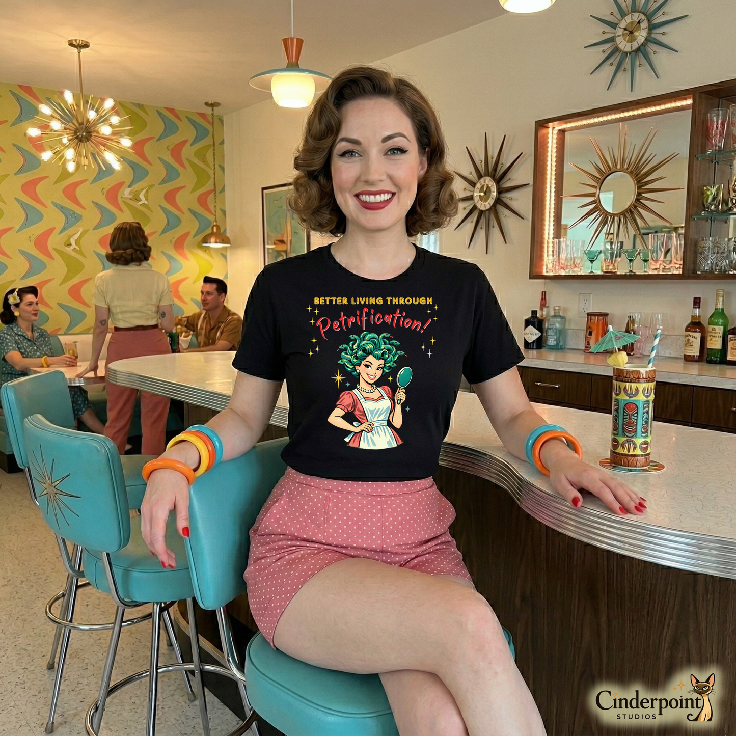 Better Living Through Petrification unisex tee — vintage 1950s retro Medusa housewife with styled snake hair holding a hand mirror and smiling confidently in pearls and apron, gold and red typography on black Bella Canvas 3001 by Cinderpoint Studios