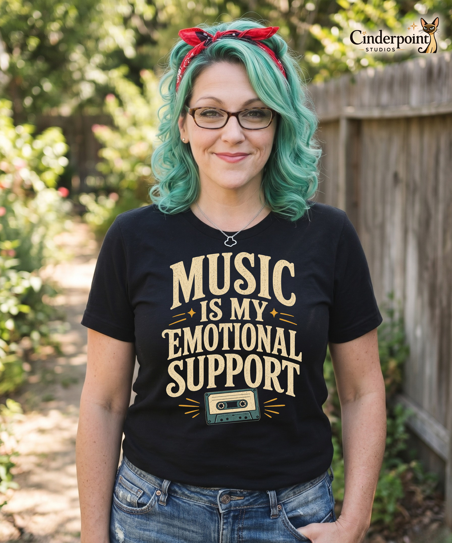 Auntie Mel, the designer, wearing a black graphic tee with the Music Is My Emotional Support design by Cinderpoint Studios, featuring retro lettering, star accents, and a cassette tape graphic.