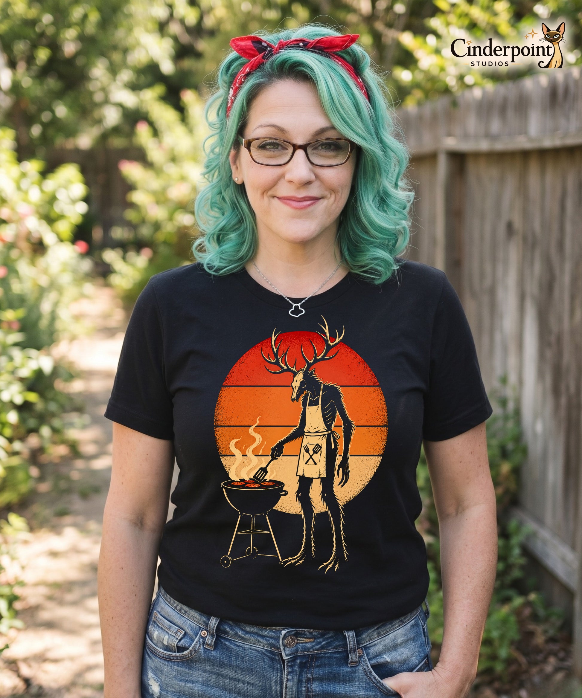 A retro-style graphic t-shirt featuring a Wendigo cryptid with antlers wearing a BBQ apron and grilling at a spatula, set against a vibrant 1980s neon sunset background.