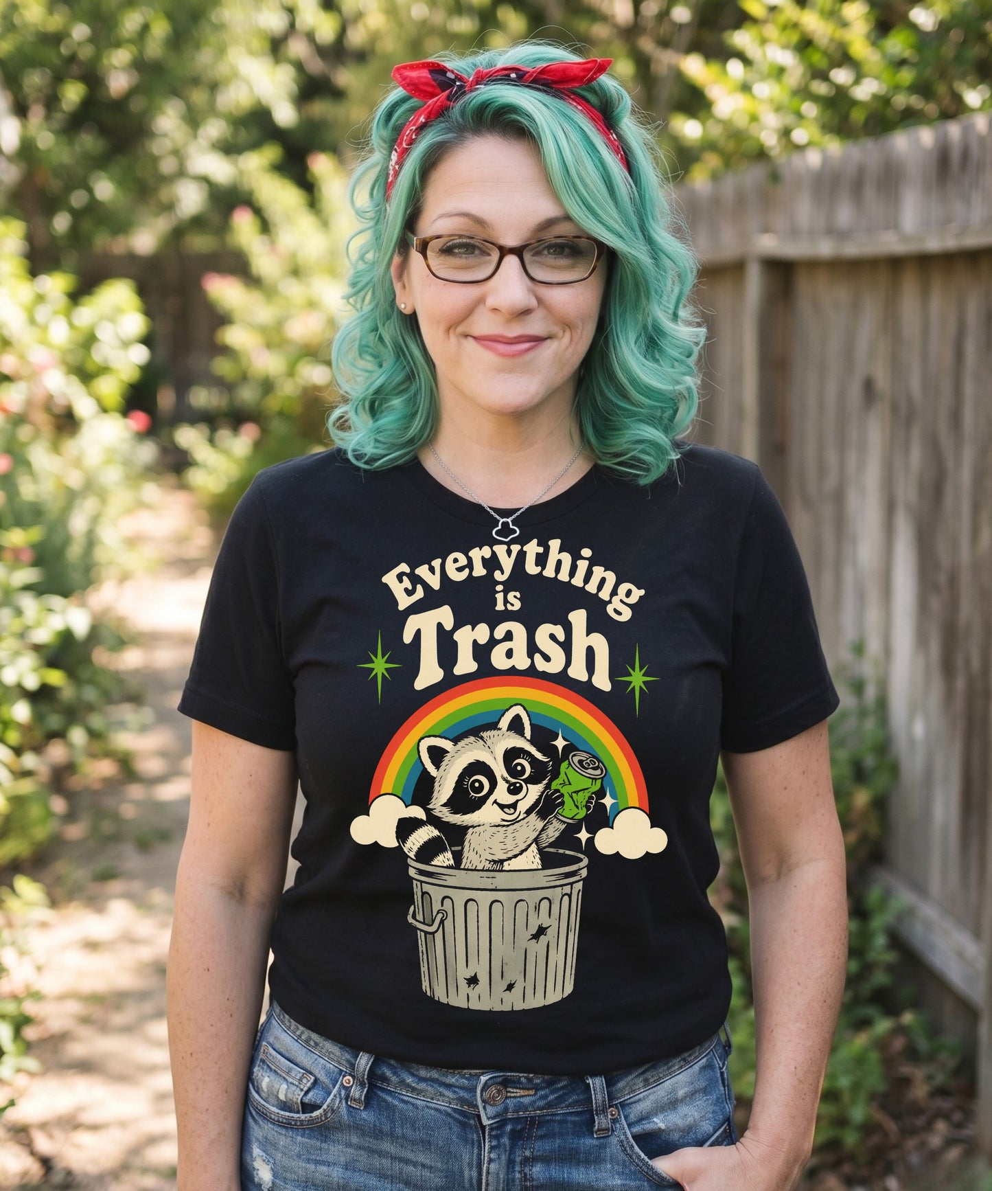 A retro 1970s-style graphic t-shirt featuring a cute raccoon sitting under a vibrant rainbow with the text "Everything Is Trash" in vintage-inspired lettering