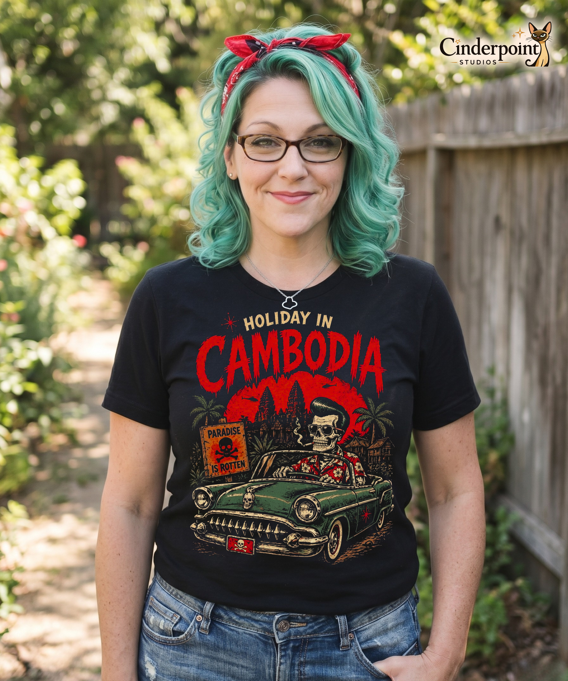 A detailed lowbrow graphic on a black t-shirt featuring a skeleton with a pompadour driving a 1955 Chevy convertible. The background shows Angkor Wat under a red sun with helicopters, and a sign that reads 'Paradise is Rotten'.