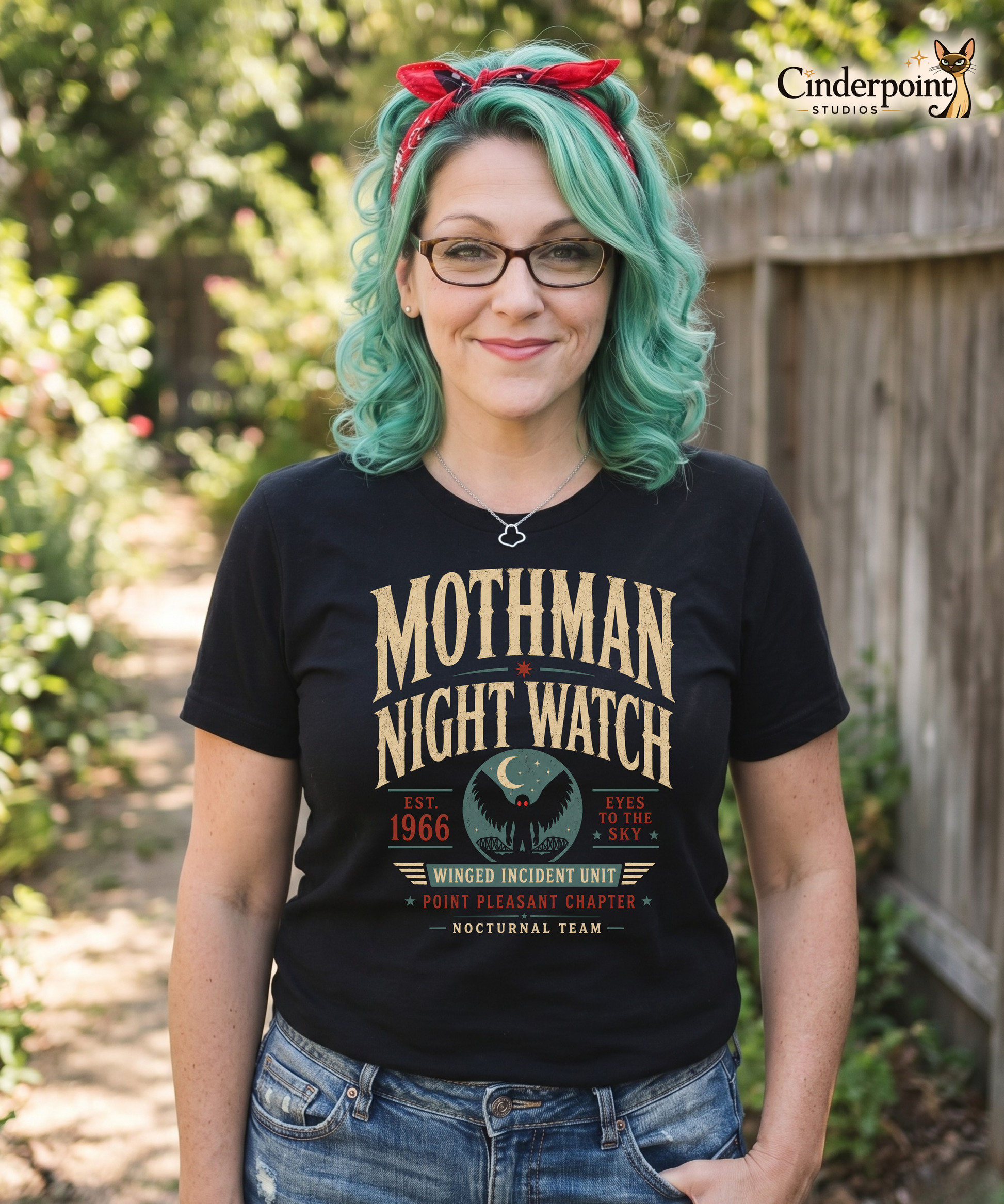 Auntie Mel wearing a black graphic tee with the Mothman Night Watch design by Cinderpoint Studios, featuring retro cryptid artwork, Mothman silhouette, bridge imagery, and Point Pleasant-themed details.